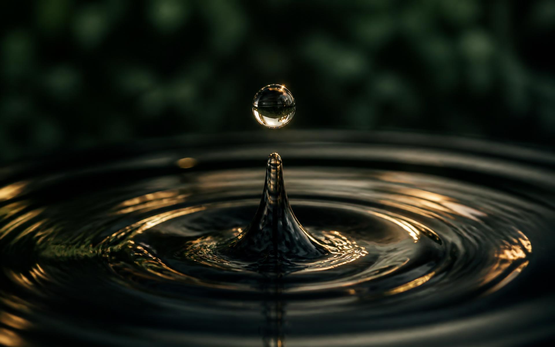 Water droplet suspended above a dark rippling surface with gold highlights